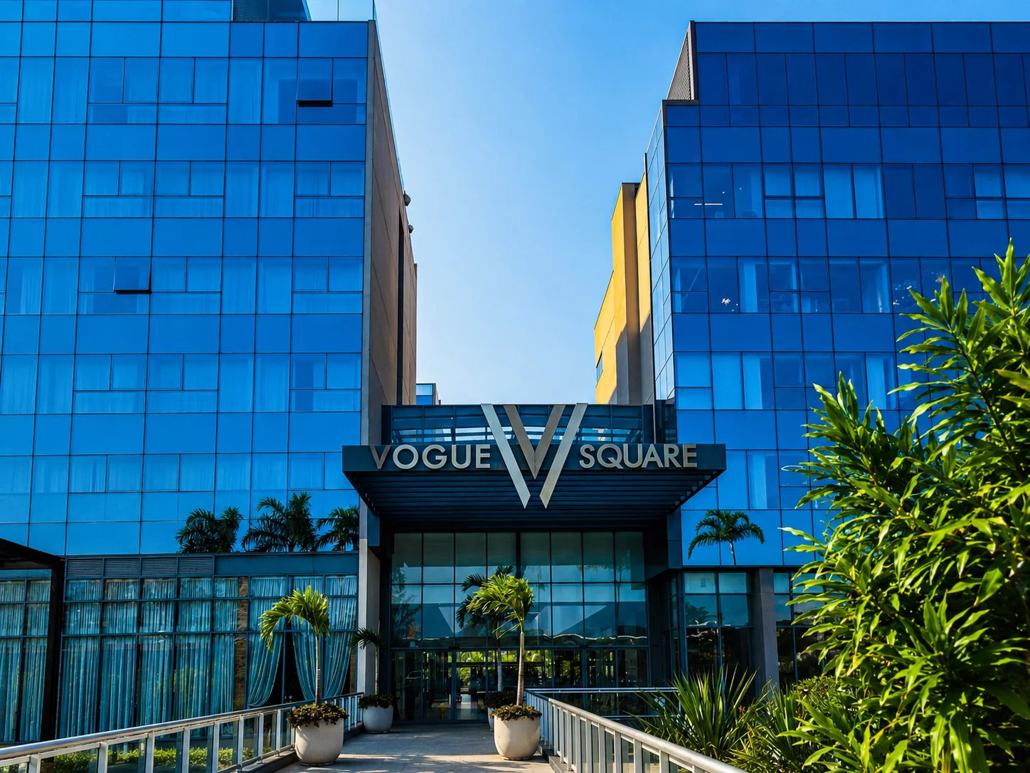 Fachada e entrada principal do Vogue Square — marquise na entrada, palmeiras e torres de vidro